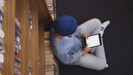 Asian-female-student-wearing-a-blue-hijab-sitting-on-the-floor-and-using-tablet