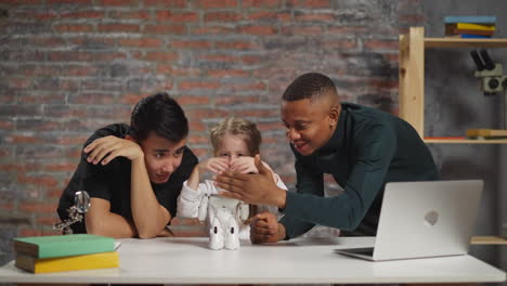 little girl and black man wave hands to move robot in studio