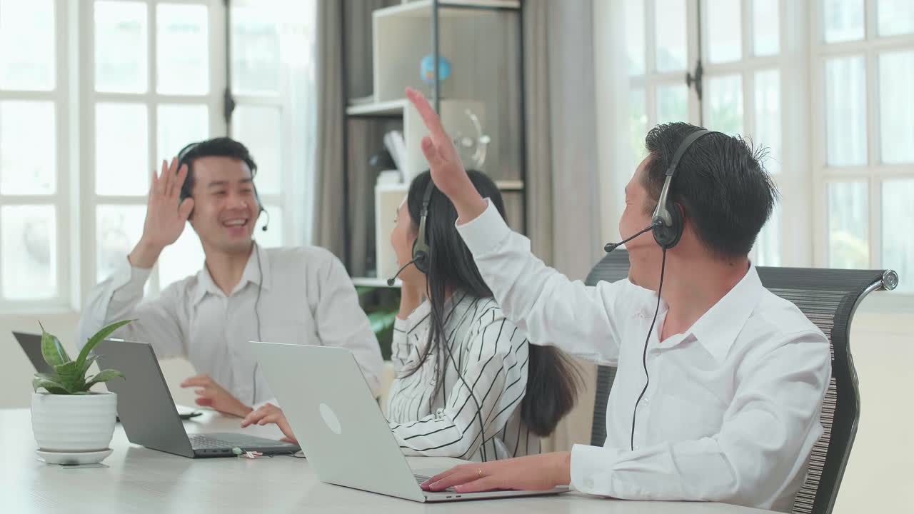 Three Asian Call Center Agents Wearing Headsets And Being Happy Due To Success Working With Computers At The Office