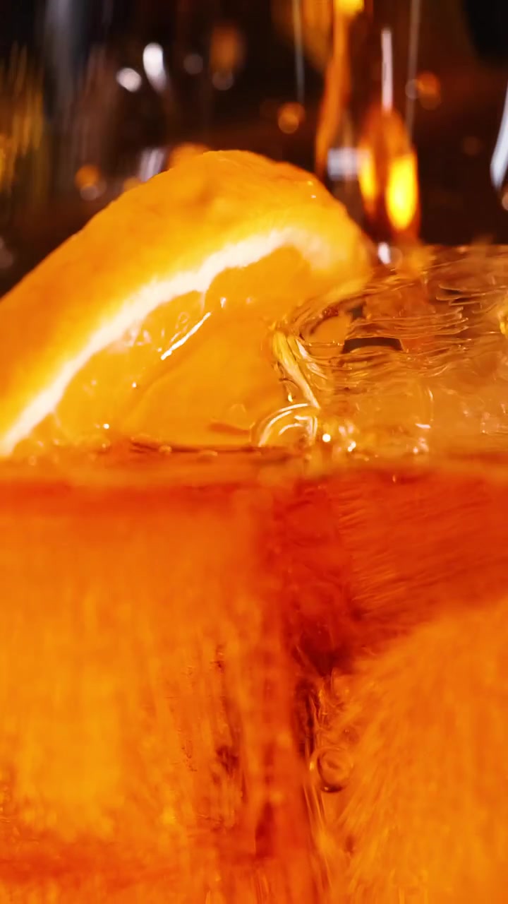 Una bevanda arancione vivace riempie un bicchiere pieno di cubetti di ghiaccio e una guarnizione di agrumi.
