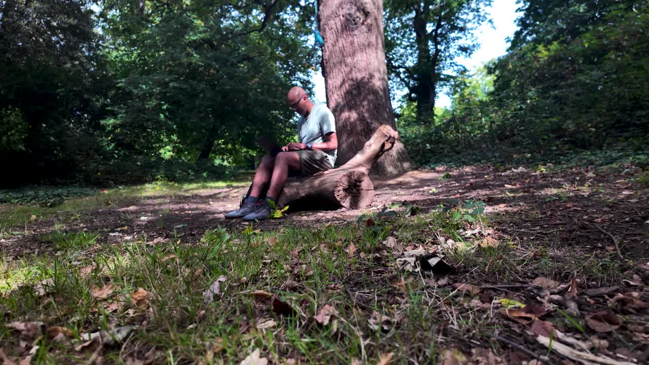 South Asian man using laptop on log, working outdoors in the forest