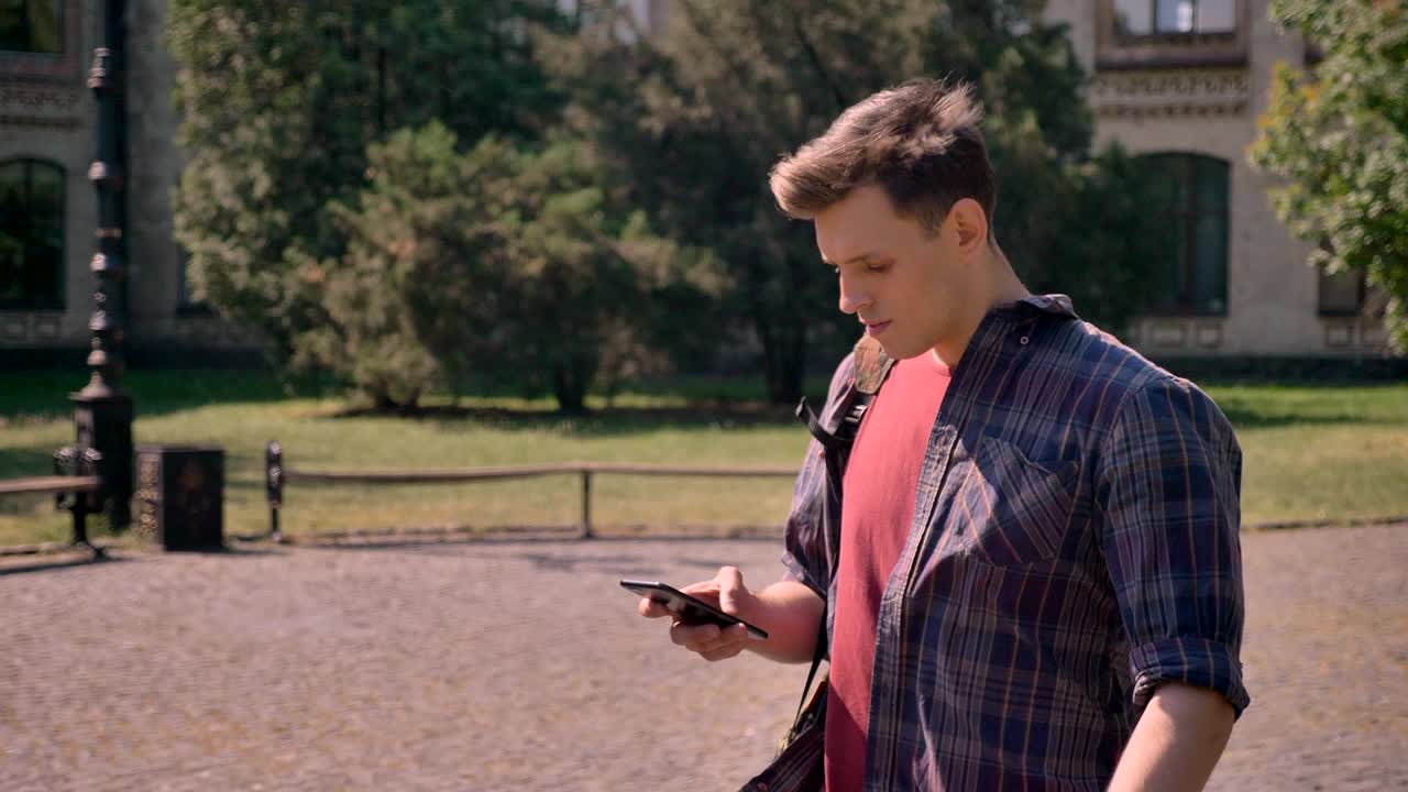 매력적인 젊은 남자가 여름에 낮에 공원을 걸어다니며 스마트폰, 통신 개념을 하고 있습니다.