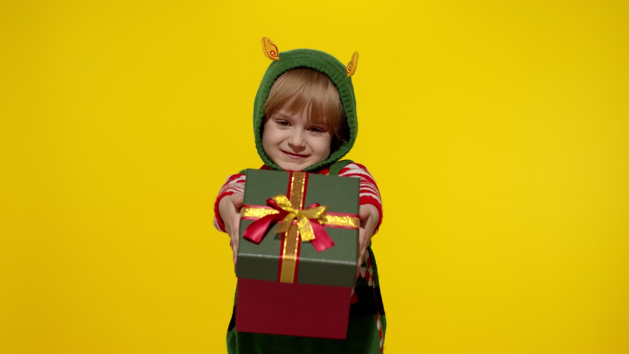 Dívka jako vánoční skřítek, pomocník Santa Clause, dává dárkovou krabici do kamery. Šťastné novoroční svátky.