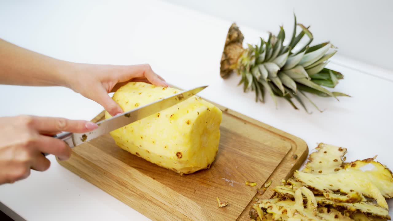 Fresh peeled pineapple on a wooden board. Woman's hands holding sharp knife and cleaning pineapple on the table.