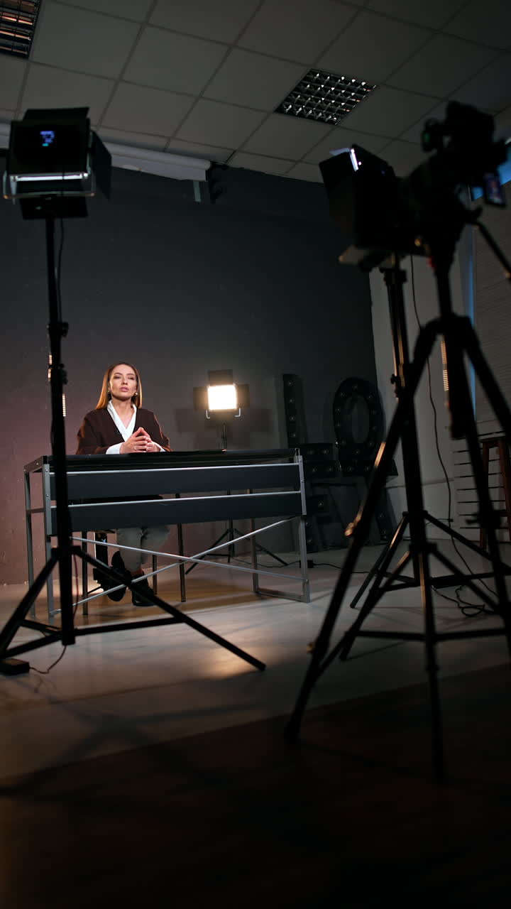 Lady with long hair sits in studio surrounded by soffits. Low angle view at the blogger filming a video. Vertical view.