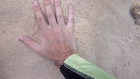 A-hand-slamming-on-the-sandy-bottom-of-Koh-Kradan,-Thailand---underwater