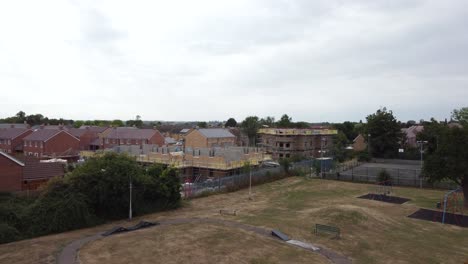 Drone-approaching-building-development-site-whilst-passing-over-a-tree-in-a-park-from-a-medium-angle-in-Bedfordshire,-England-uk,-on-a-cloudy-day