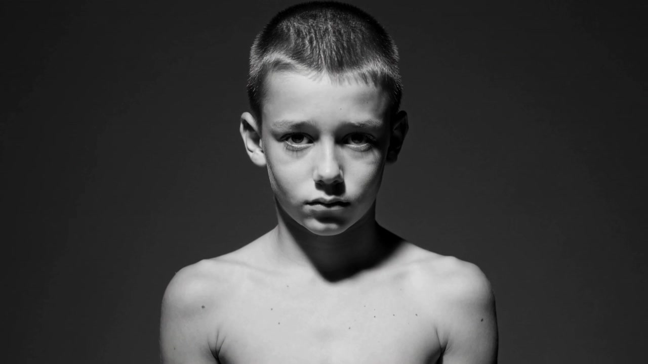 Início da gravação, adolescente sem camisa com expressão neutra em estúdio para um retrato sob luz superior.