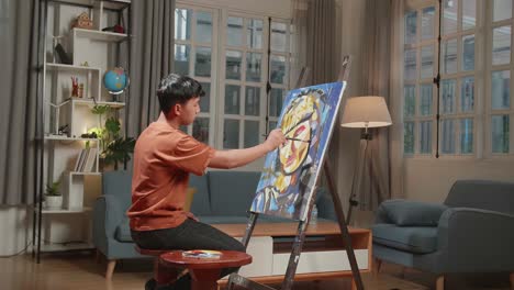 asian artist boy sitting on round wooden chair without backrest holding paintbrush mixed colour and painting a girl's hair on the canvas