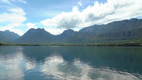 ripples of the surface of lake annecy reflects clouds and tips of the nearby mountains