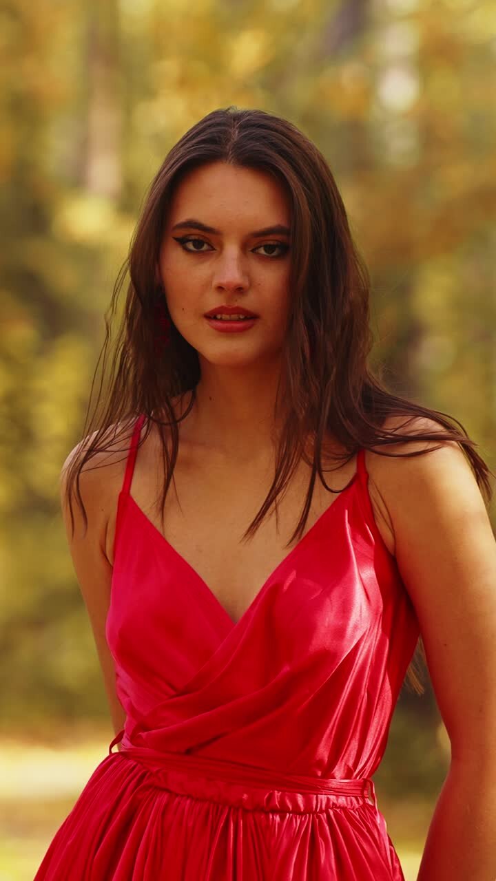 Eleganza accattivante: una modello in un impeccabile abito di raso rosso posa con grazia all'aperto, circondata dai colori autunnali, mettendo in mostra bellezza e sicurezza
