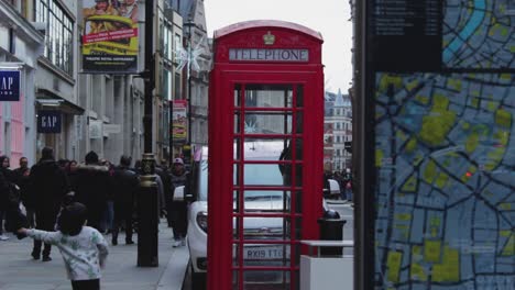 red telephone box in the city center in london. united kingdom. peolple passing by a traditional telephone kiosk on sidewalk, london map on the foreground