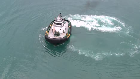 areial close up view of a tugboat, in the calm carribbean waters, as it maneuvers into position to assist an ocean vessel leaving port