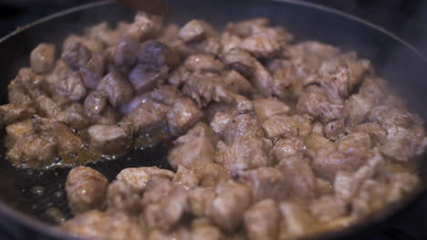 wooden spoon stirring sizzling diced chicken pieces in hot pan