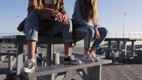 mid section view of a caucasian and a mixed race girl talking sitting on a table