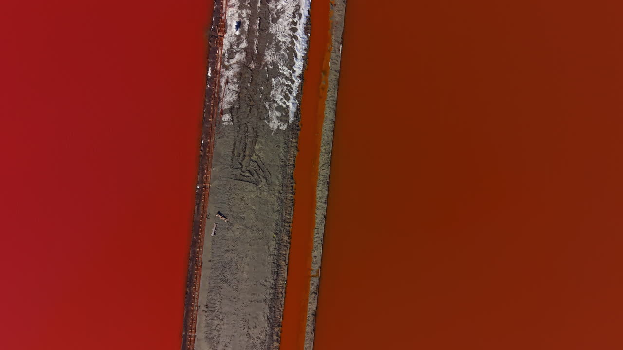 Bright red salt flats with water channels and sand pathways taken from above in a coastal area during daylight