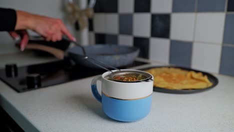 Slow motion flip of pancake behind steaming herbal tea in cozy kitchen light