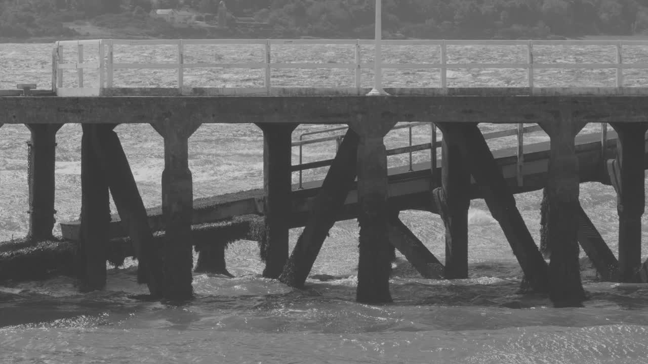 Static grayscale shot of wooden pier and ramp over rough firth waters, overcast natural lighting