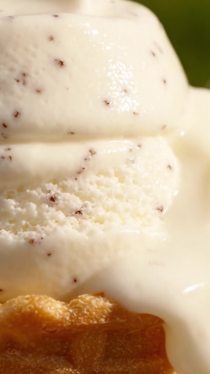 Delicioso primer plano de helado cremoso derritiéndose sobre un crujiente cono de waffle, capturando un postre de verano perfecto con rico sabor a vainilla y remolinos de chocolate.