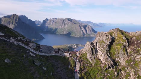 mountain hikers walking uphill following a stony staircase trail to reinebringen peak, people enjoy a breathtaking panorama of reine village and lofoten islands from mount ridge viewpoint