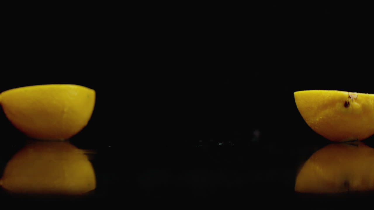 limón amarillo cortado caer en 2 partes de vidrio con salpicaduras de agua en cámara lenta en un fondo oscuro
