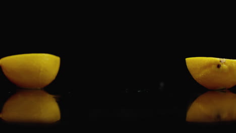 limón amarillo cortado caer en 2 partes de vidrio con salpicaduras de agua en cámara lenta en un fondo oscuro