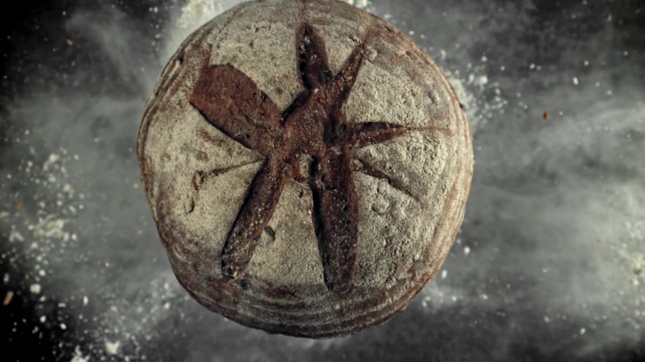 Vista dall'alto di pane rustico con farina che cade su sfondo scuro