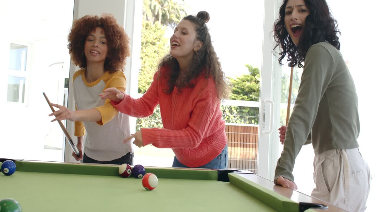 Diverse women advising shot on green-felt pool table in game room for fun, striking balls cheering