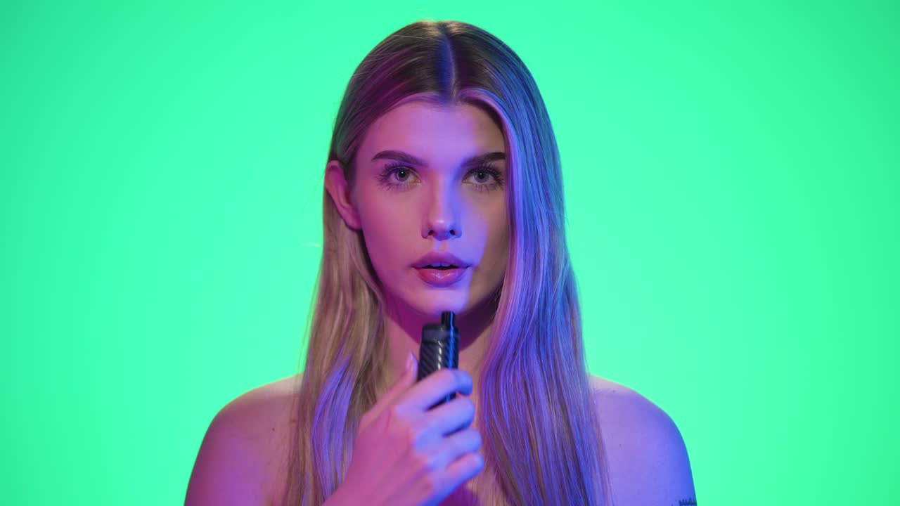 disparo medio de una mujer joven y bonita tomando un tirón en un vaporizador electrónico o narguile electrónico y exhalando el humo frente al fondo verde en cámara lenta