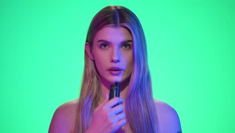 disparo medio de una mujer joven y bonita tomando un tirón en un vaporizador electrónico o narguile electrónico y exhalando el humo frente al fondo verde en cámara lenta