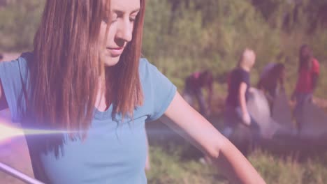 video de luces sobre una feliz mujer caucásica recogiendo basura con voluntarios en el campo