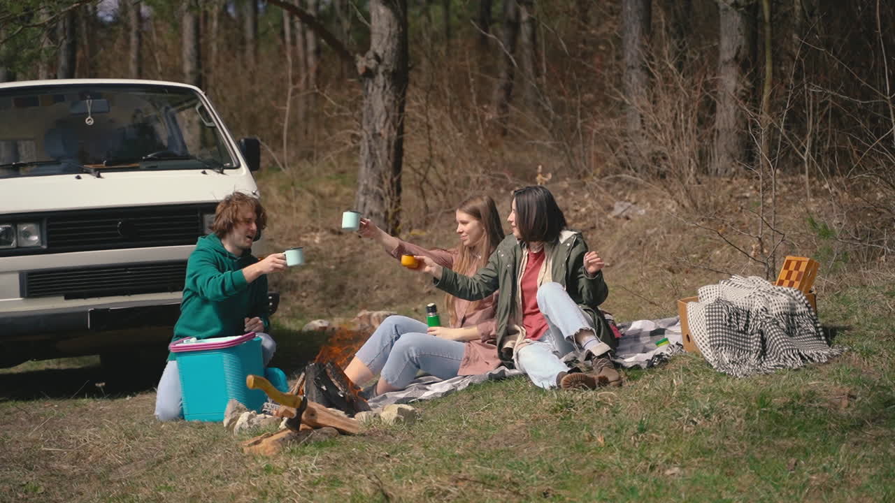 Free stock video - Two young girls and a young boy have a good time in the forest having a hot beverage 1