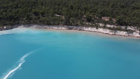 una toma aérea dinámica desde una gran altura de la bahía que desciende hacia la orilla del mar pasando una moto de agua rápida que deja rastros de agua