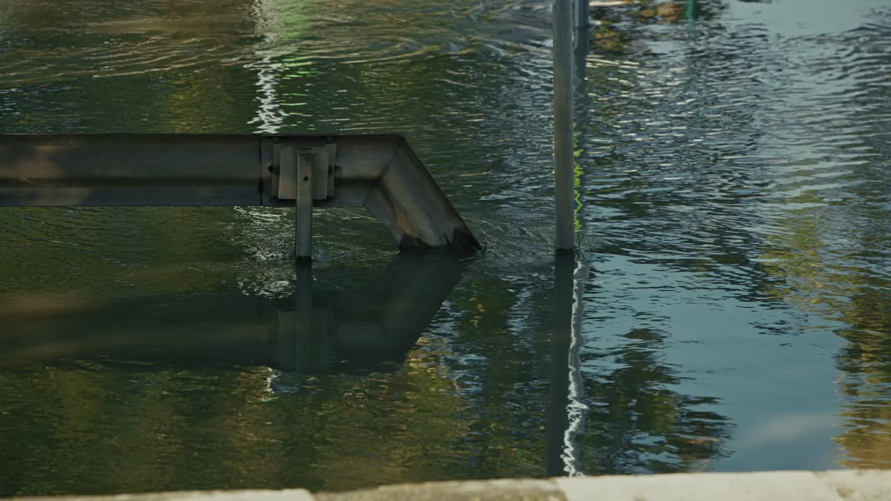 Water flowing from a metal pipe into a calm body of water
