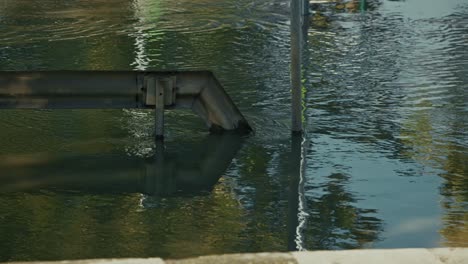 water flowing from a metal pipe into a calm body of water