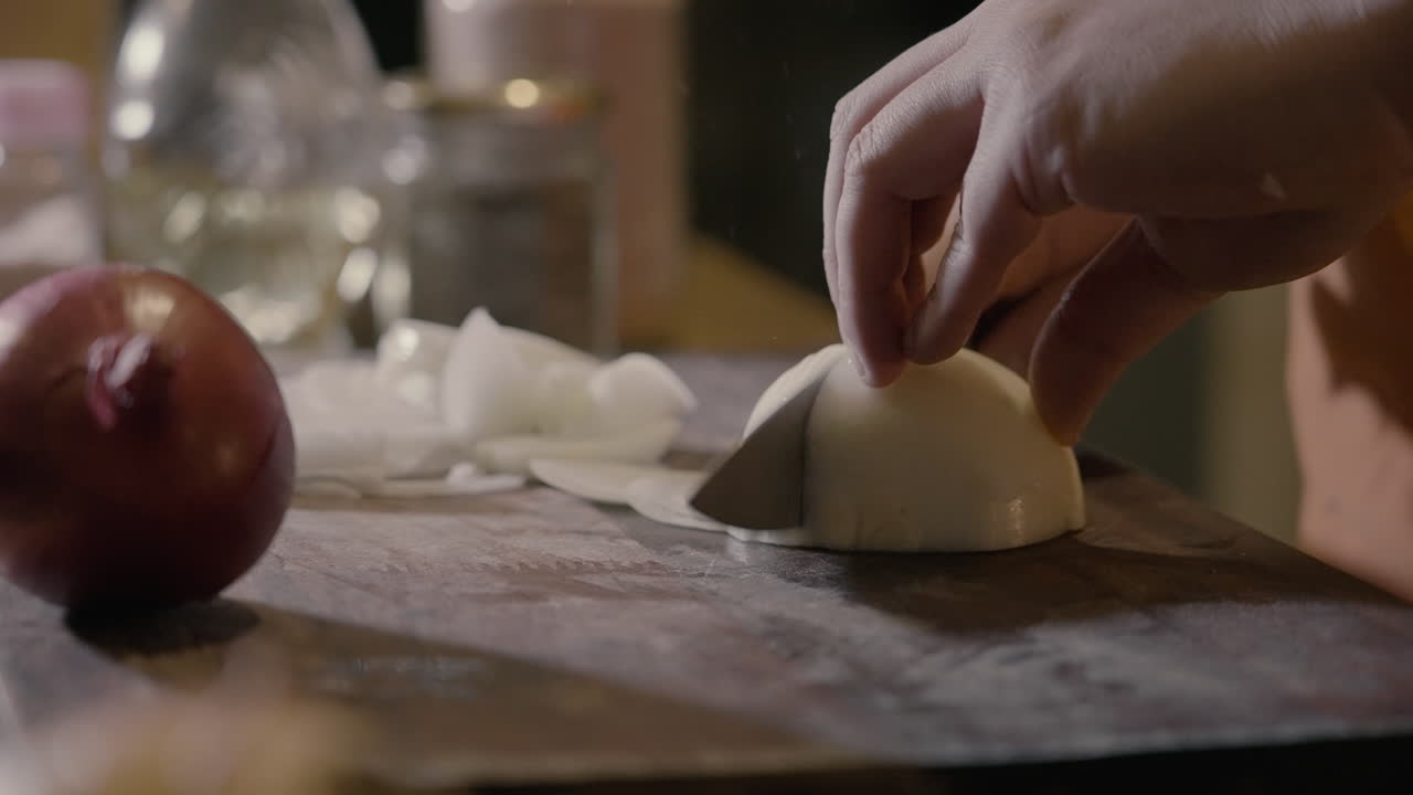 Primo piano di mani che affettano una cipolla bianca su un tagliere di legno