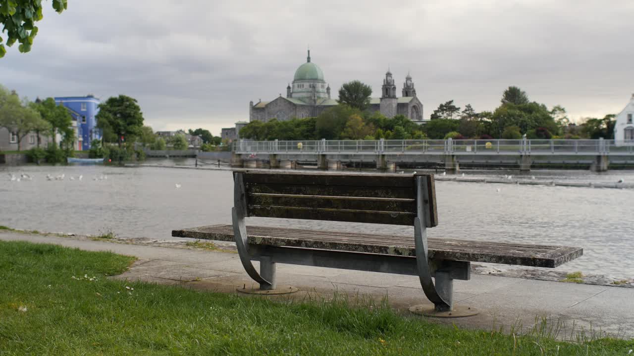 Galway girl in grey jumpsuit walks past old bench along canal riverwalk in Ireland