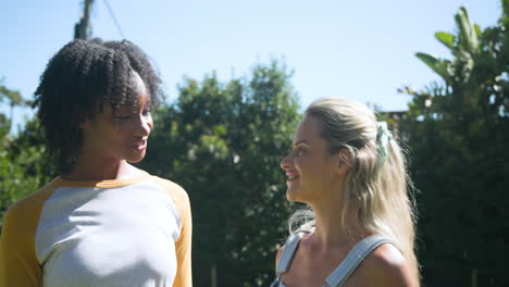 two female friends enjoying conversation outdoors on sunny day by pool