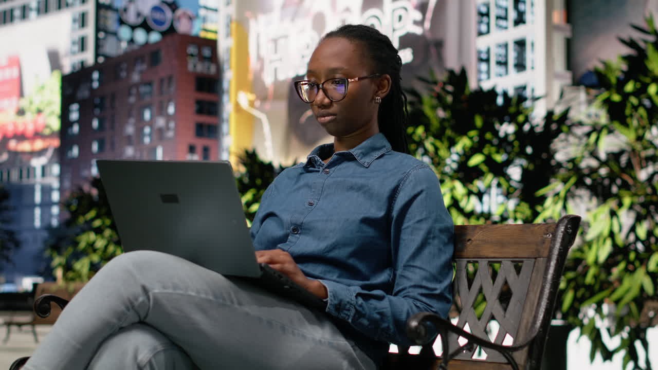Smiling black woman sitting outside, using laptop to solve tasks and study data