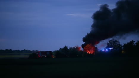 large fire burning out of control at the field in zlotoryja, poland during twilight. firetrucks arrived at the site - wide shot