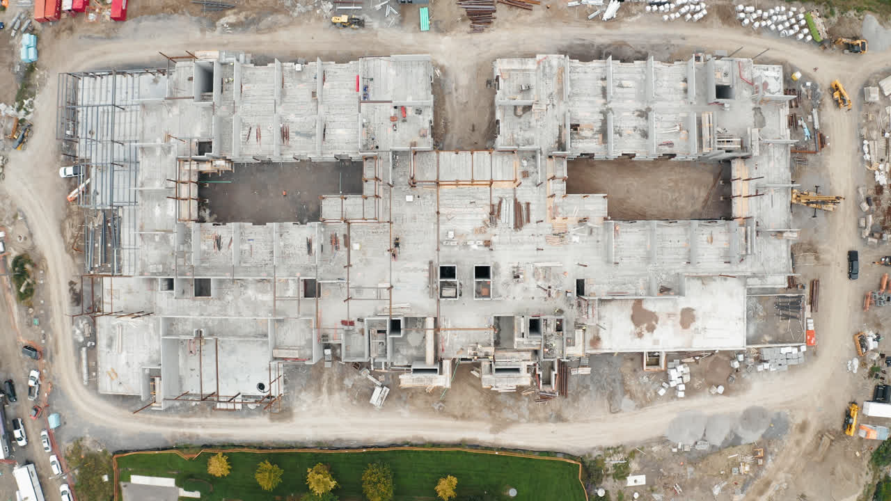 vuelo aéreo de vista superior sobre un nuevo edificio comercial en desarrollo con trabajadores del sitio de construcción sindical empleados que operan trabajos de maquinaria pesada viviendas industriales urbanas inmobiliarias 4k