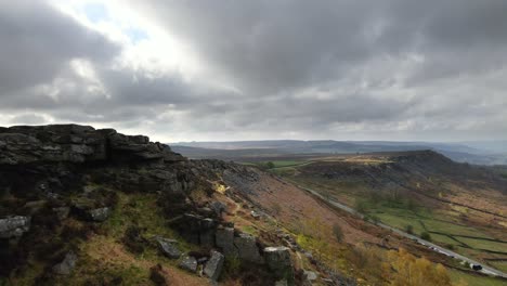 Cinematic,-aerial-drone-footage-flying-along-a-dramatic-rock-formation-with-vast-moorland-and-beautiful-sunlight