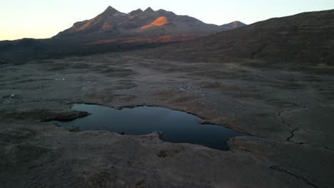 Flying-towards-Black-Cuillin-mountains-at-sunrise-over-dark-reflective-loch-at-Sligachan-on-the-Isle-of-Skye-Scotland