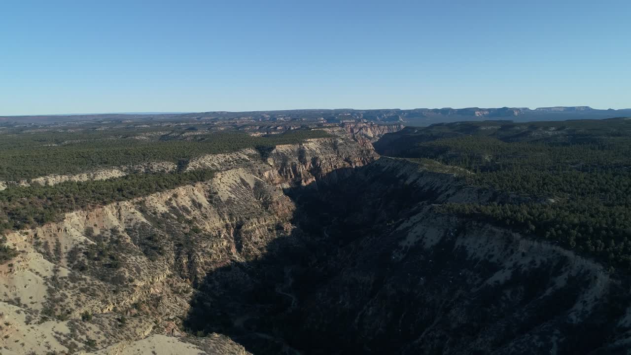 drone aéreo ascendente disparado mirando hacia abajo sobre el vasto cañón del valle del río en utah con cañones en la distancia contra el cielo azul claro en el día