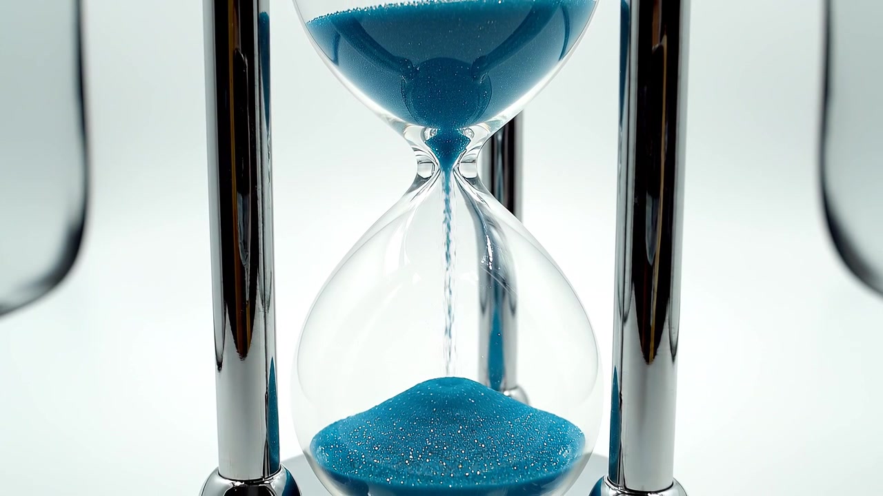 Macro of hourglass with blue sand flowing on white background