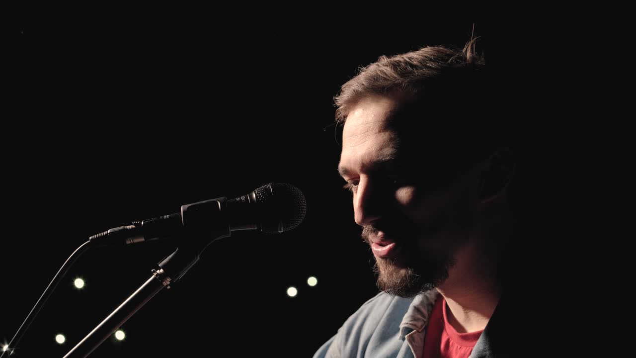 un músico está tocando la guitarra en un gran escenario con miembros de la audiencia sosteniendo linternas en el fondo. el auditorio está lleno de hermosas luces parpadeantes.