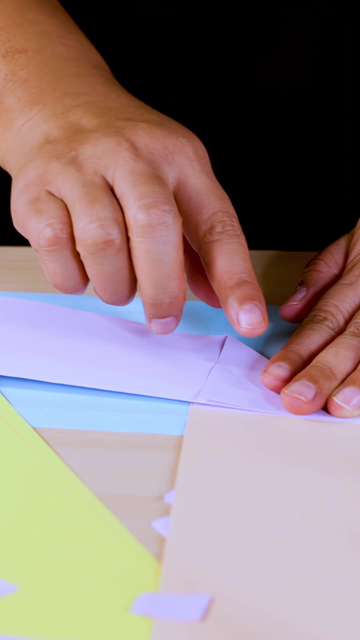 Adult hands carefully fold white origami paper on a bright, colorful table under soft lighting
