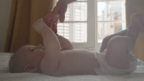 adorable baby in bed holding mother hand playful mood in soft light bedroom