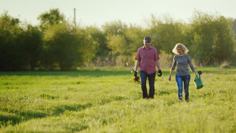 A-Young-Couple-Of-Farmers-Walking-Along-A-Country-Road-Near-A-Green-Field