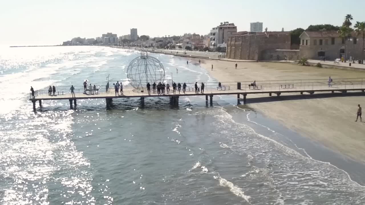 drone volando sobre una cresta de madera construida en una playa de arena donde la gente disfruta del paisaje marino, europa, chipre